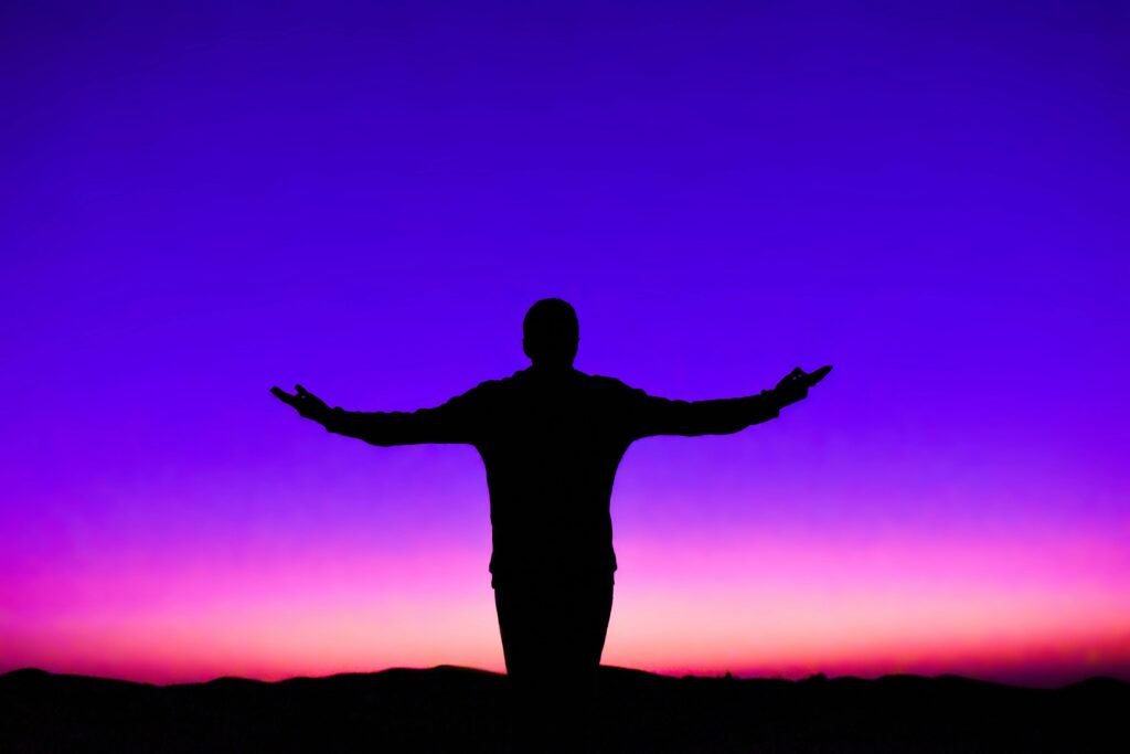 Silhouette of a person with outstretched arms against a vivid sunset sky.